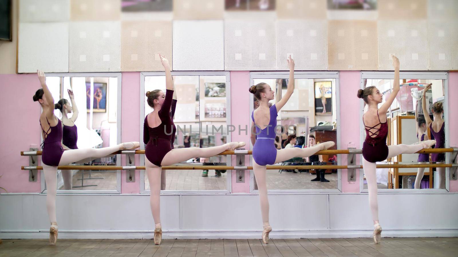 in ballet hall, Young ballerinas in purple leotards perform part de bra with a slope, bend back, tilt back, moving hands elegantly up and down, standing at railing in hall. High quality photo
