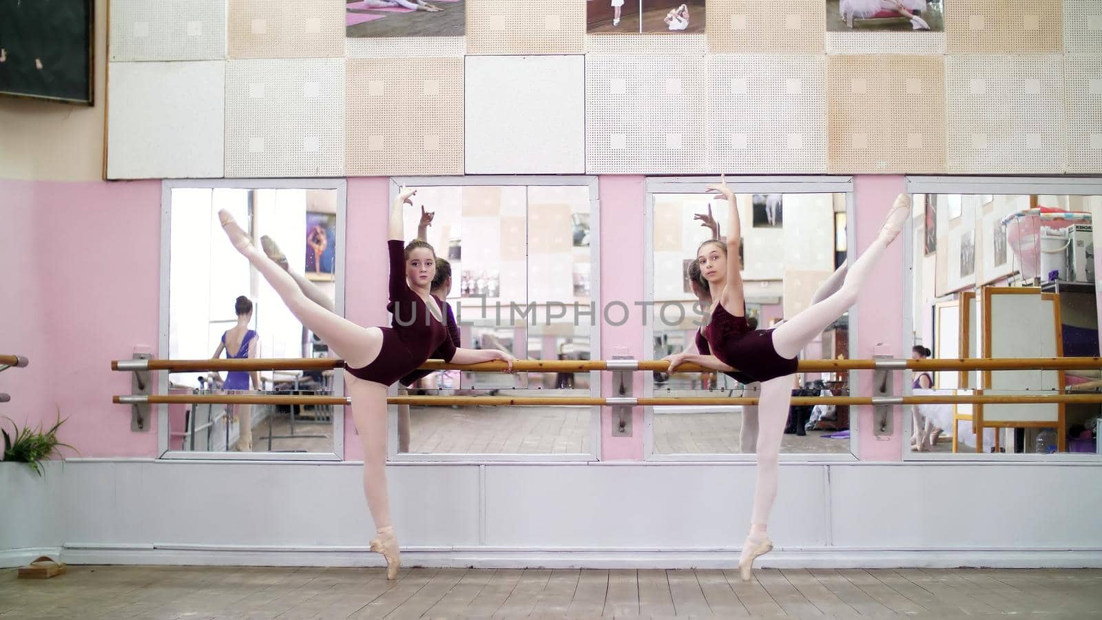 in dancing hall, Young ballerinas in purple leotards perform grand battement back on pointe shoes, raise their legs up elegantly, standing near barre at mirror in ballet class. High quality photo