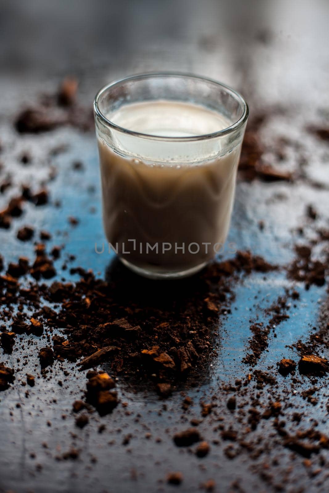 HIGH ANGLE SHOT OF GLASS OF MILK WITH SOME COCOA POWDER SPRINKLED ON BLACK GLOSSY SURFACE.