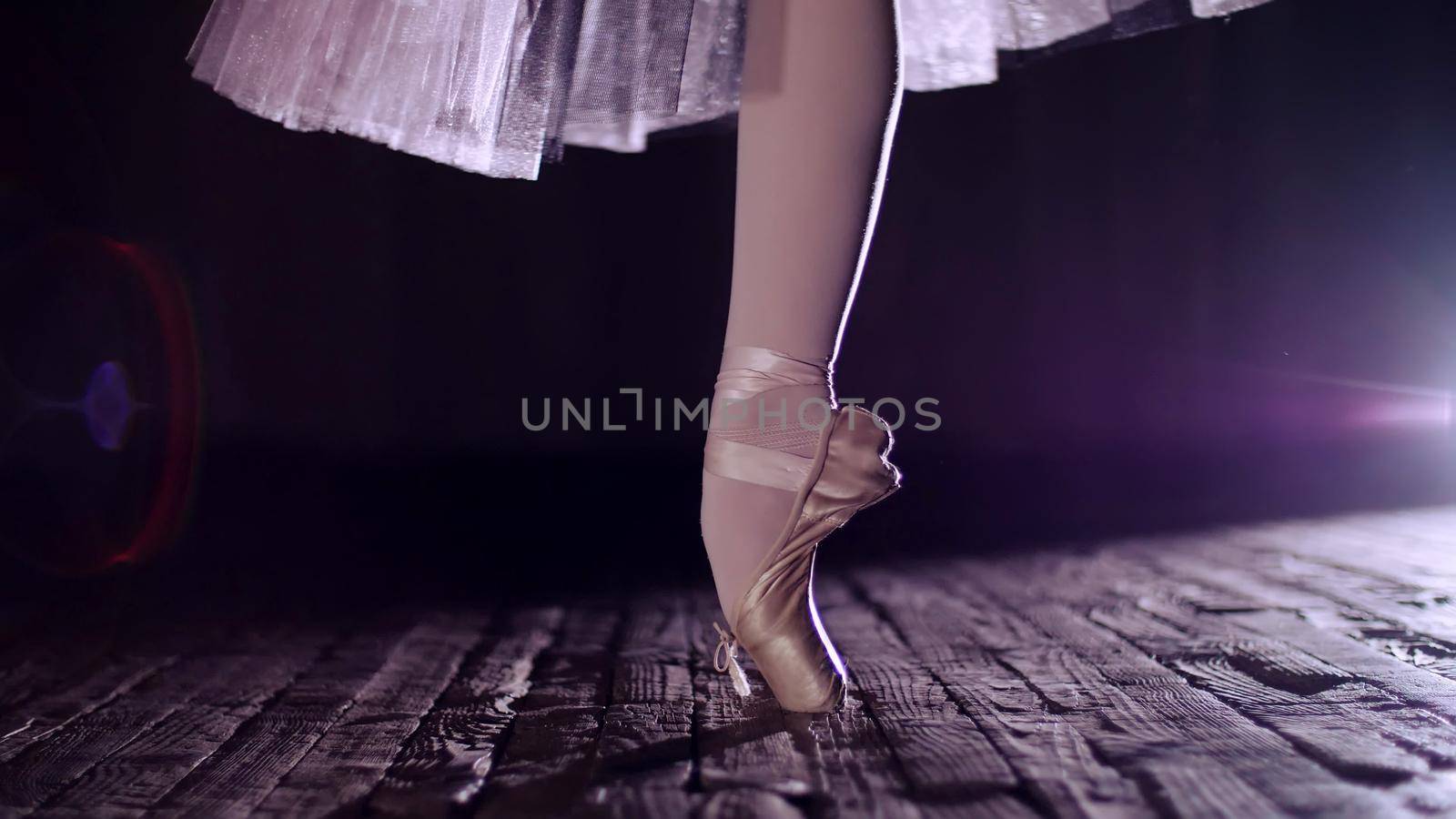 close up, in rays of spotlight, on stage of old theater hall. ballerina in white ballet skirt, rotates on toe in pointe shoe, performs elegantly a certain ballet exercise, tour,pointe. High quality photo