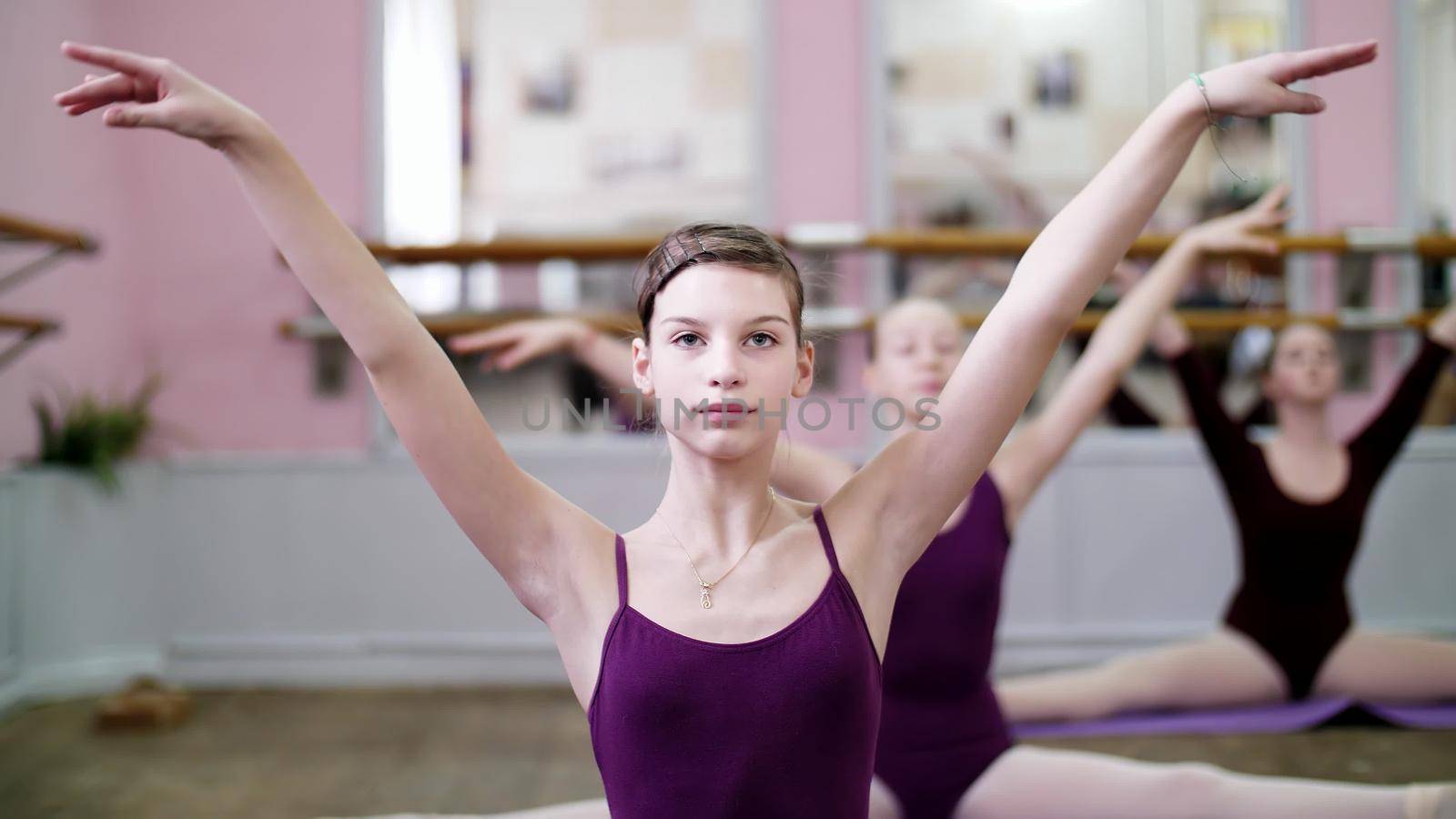 in dancing hall, Young ballerina in purple leotards performs part de bras In 3 position with forward tilt, girl is sitting on twine, moving hands elegantly , close-up by djtreneryay