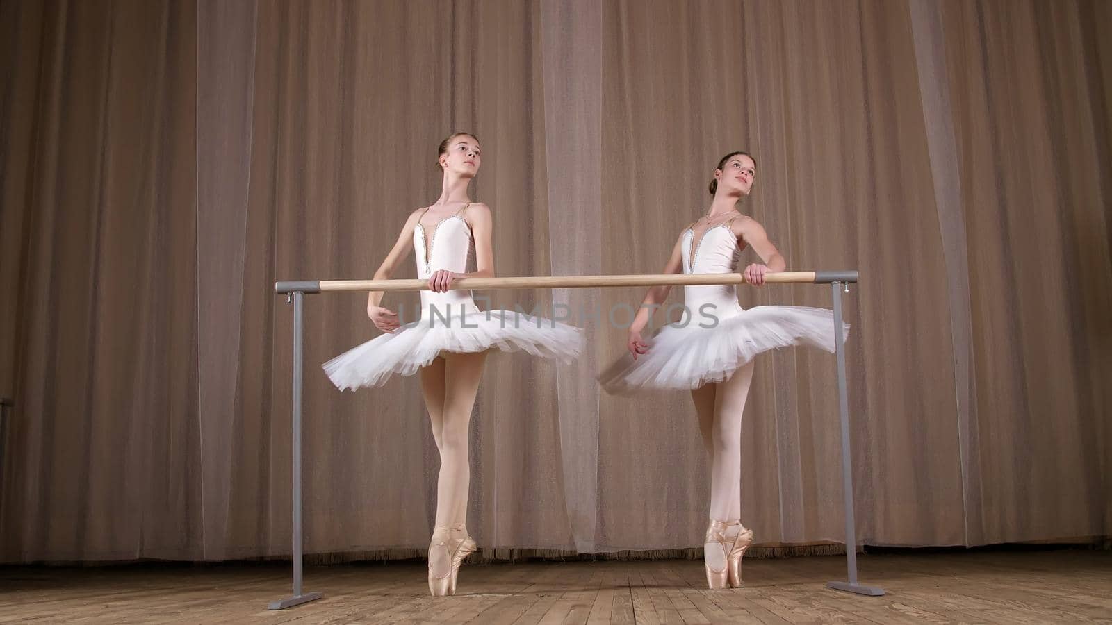 ballet rehearsal, in old theater hall. Young ballerinas in white ballet skirts, tutus, are engaged at ballet, perform elegantly a certain ballet exercise, pass , attidude, standing near barre. High quality photo
