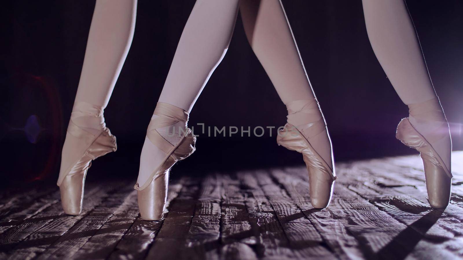 close up, in rays of spotlight, on the stage of the old theater hall. ballerinas raise on toes in pointe shoes, performs elegantly a certain ballet exercise, releve in second position. High quality photo