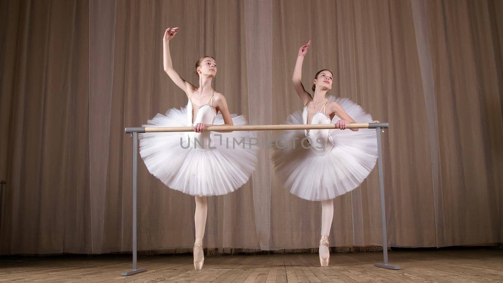 ballet rehearsal, in old theater hall. Young ballerinas in white ballet skirts, tutus, are engaged at ballet, perform elegantly a certain ballet exercise, pass , attidude, standing near barre. High quality photo