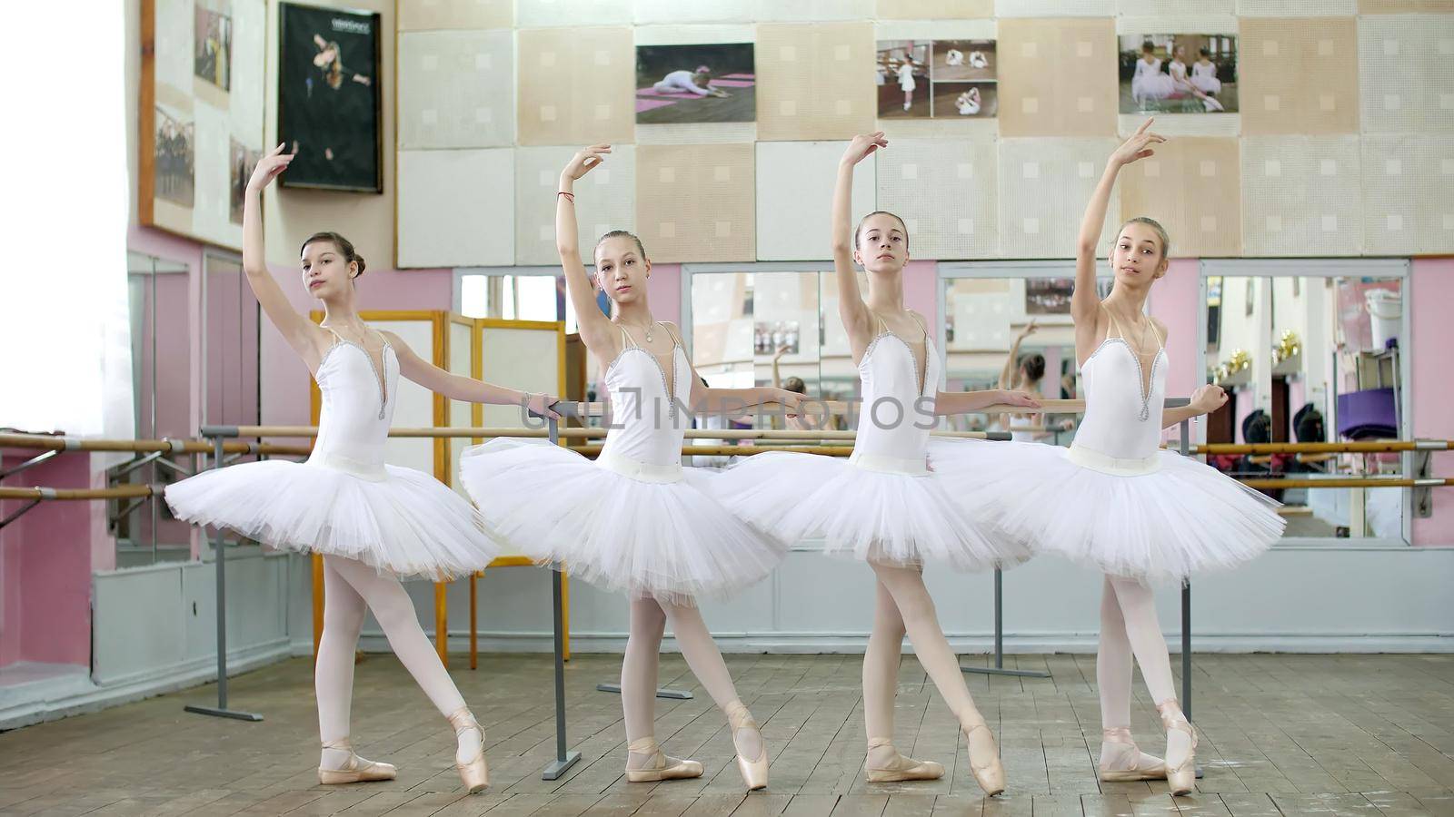 in ballet hall, girls in white ballet skirts are engaged at ballet, rehearse tendue forward battement, Young ballerinas standing in pointe shoes, at railing in ballet hall. by djtreneryay