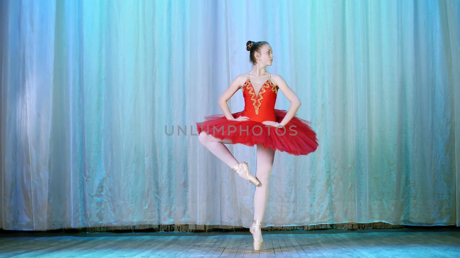 ballet rehearsal, on the stage of the old theater hall. Young ballerina in red ballet tutu and pointe shoes, dances elegantly certain ballet motion, pas courru , tour fouette. High quality photo
