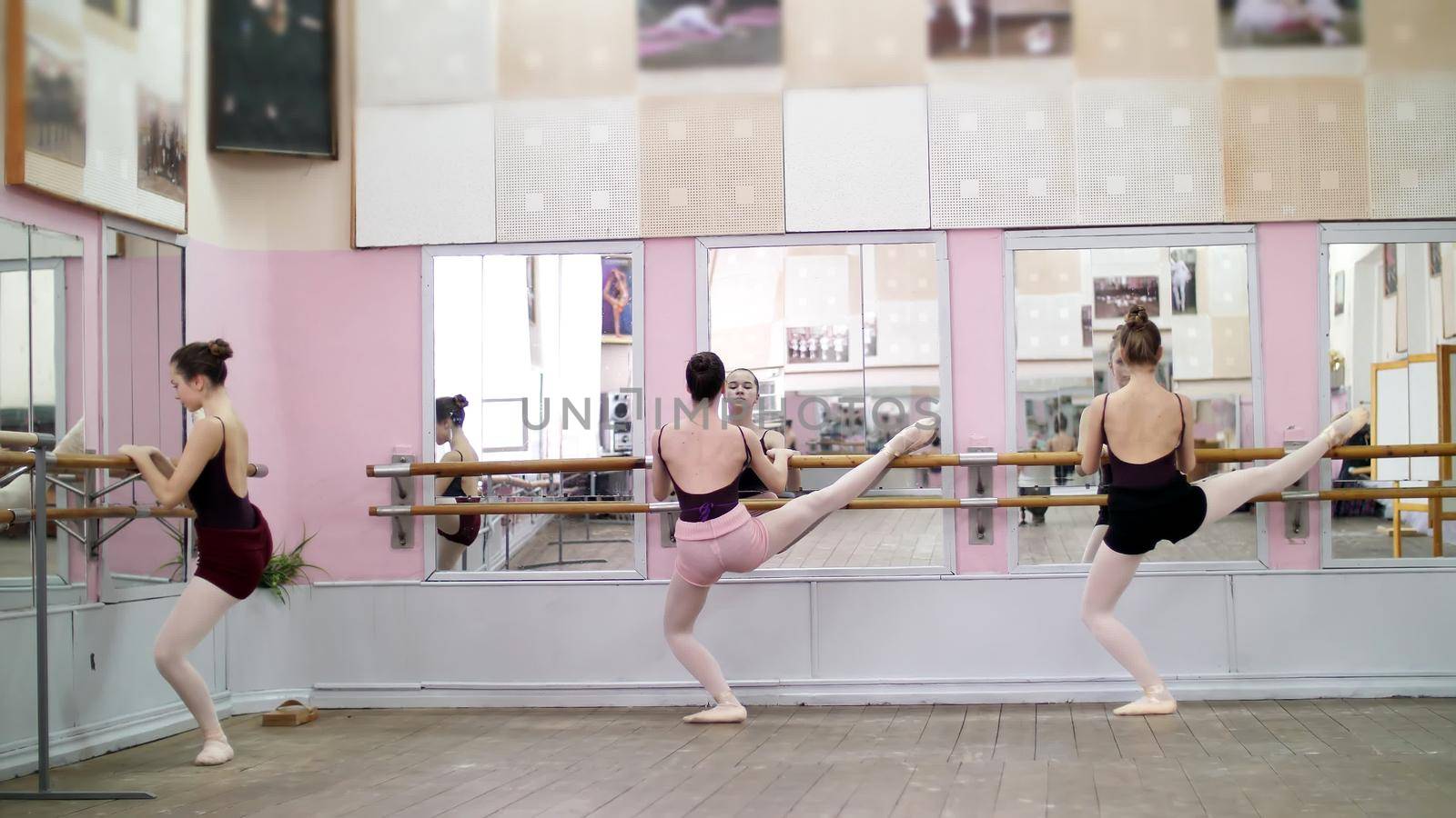 in dancing hall, Young ballerinas in black leotards stretching at barre, on pointe shoes, elegantly, standing near barre at mirror in ballet class. High quality photo