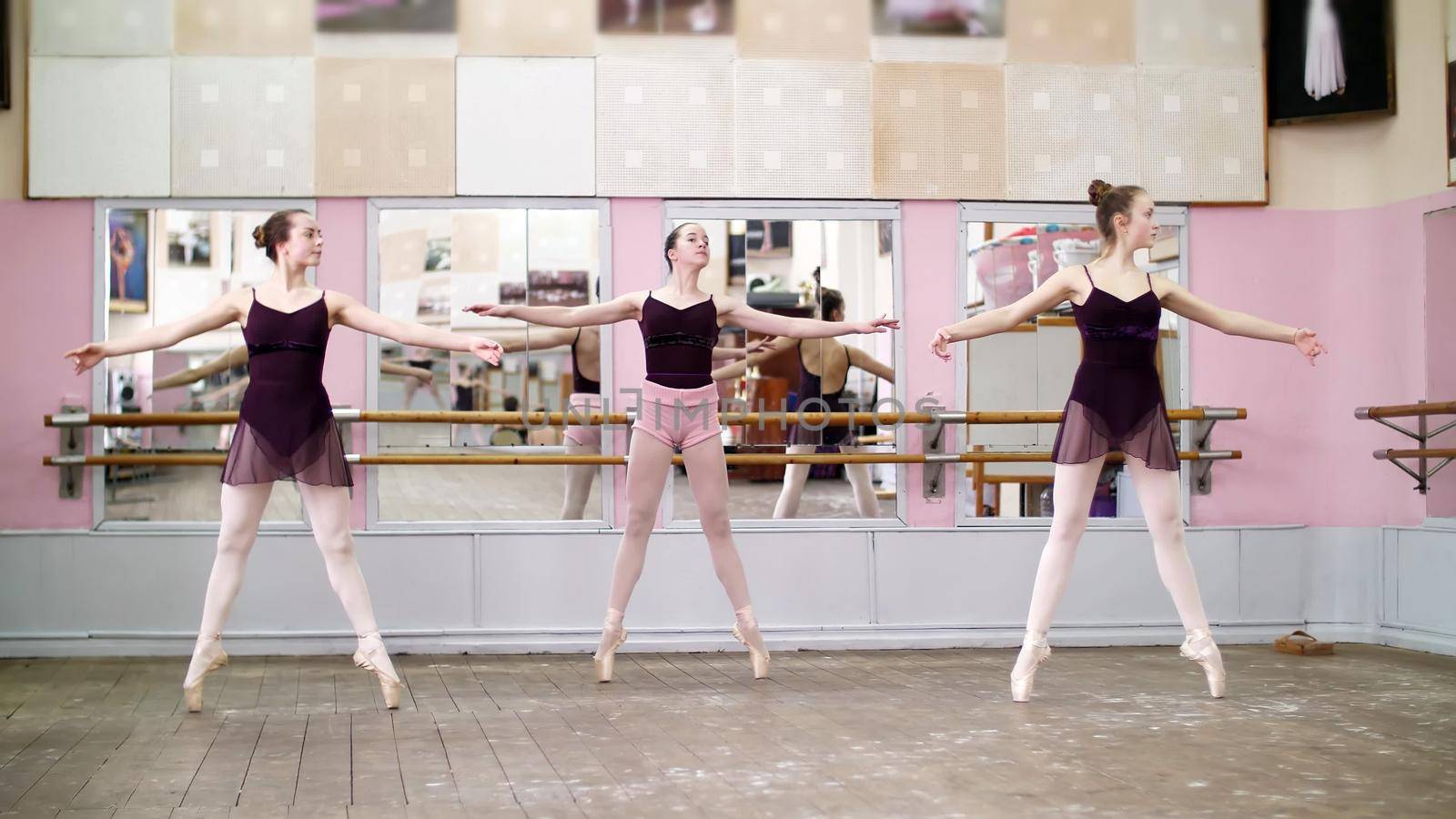 in dancing hall, Young ballerinas in black leotards perform pas echappe, standing on toes in pointe shoes near barre at mirror in ballet class. by djtreneryay