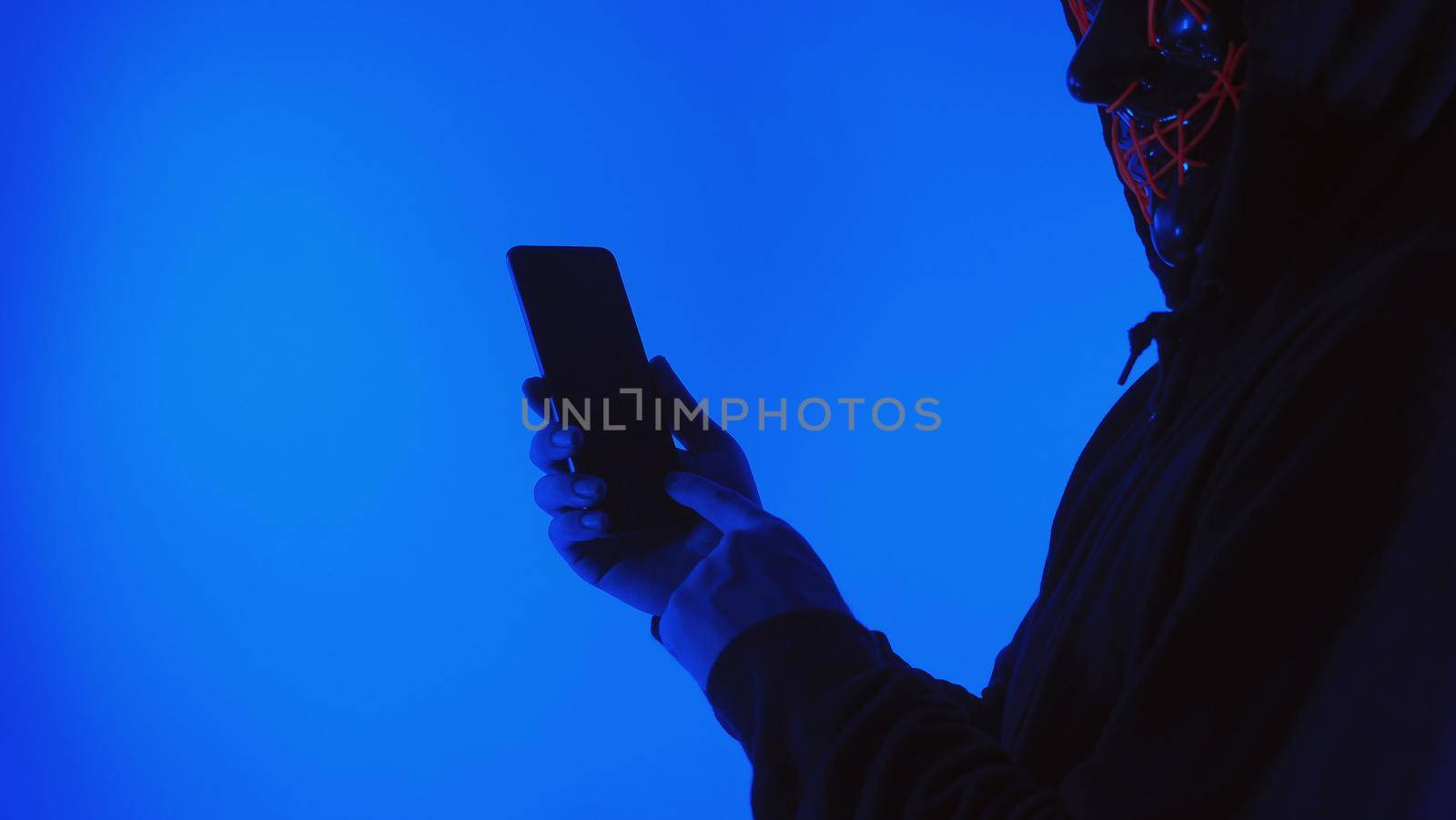 Digital security Concept. Anonymous hacker with mask holding smartphone hacked. Personal and Cyber data security in mobile phone stolen by man in mask. Represent digital privacy protection concept.