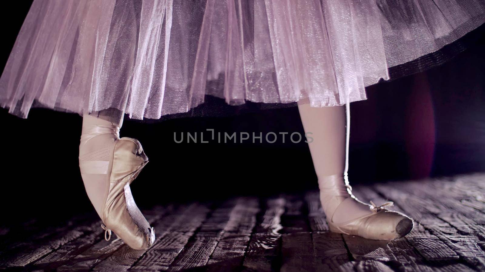 close up, in rays of spotlight, on stage of old theater hall. ballerina in white ballet skirt, raises on toes in pointe shoes, performs elegantly a certain ballet exercise, pointe ,tendu. High quality photo