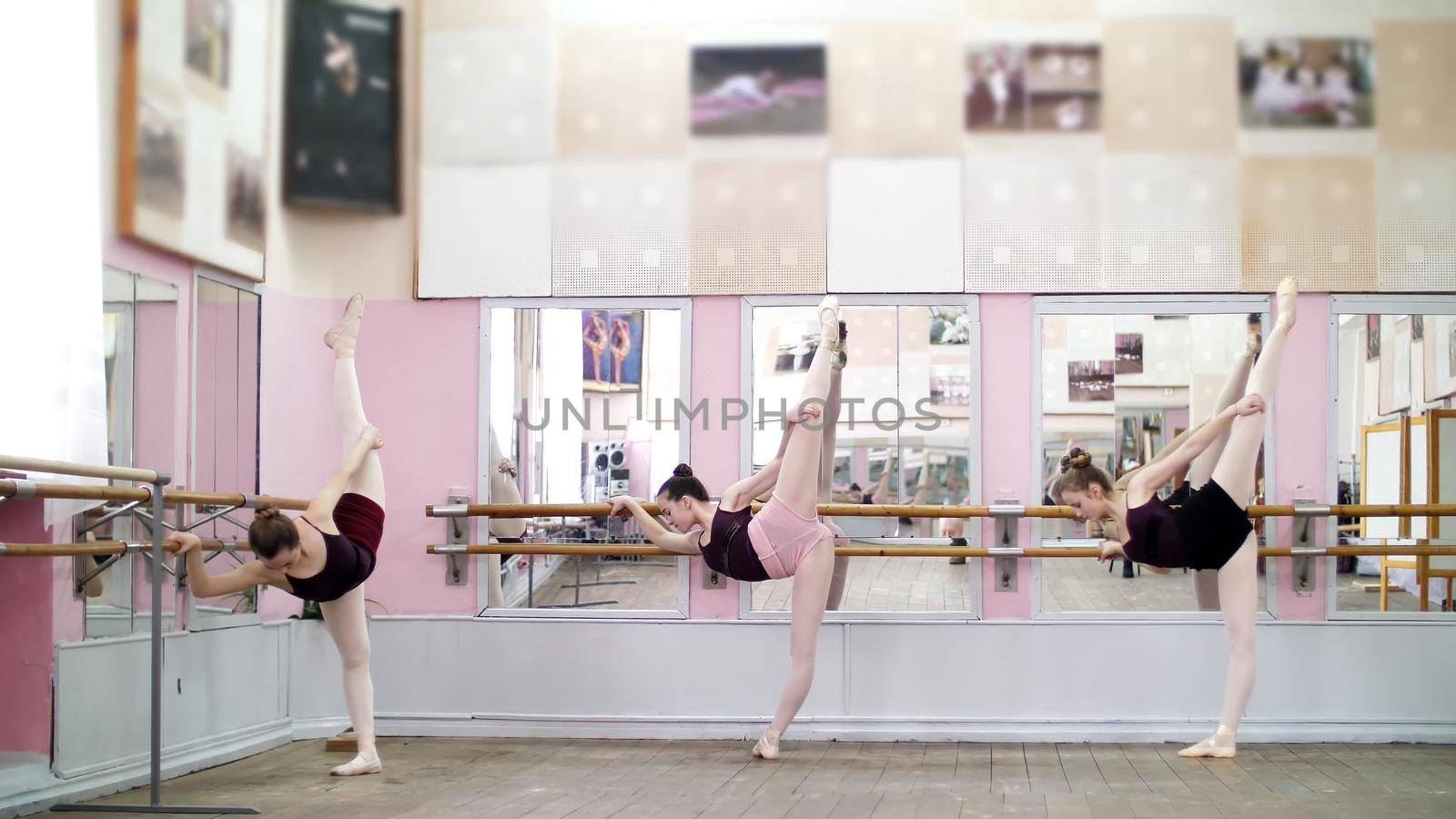 in dancing hall, Young ballerinas in black leotards are stretching, standing near barre at mirror in ballet class. by djtreneryay