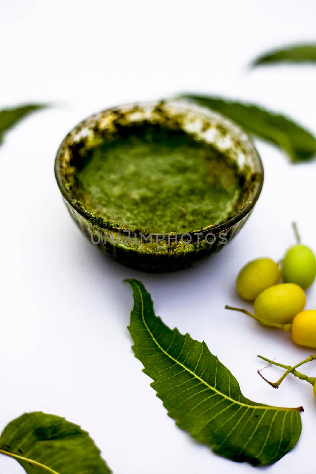 Neem paste or nim paste in a glass bowl isolated on white along with neem fruit in another bowl and some leaves also in it. by mirzamlk