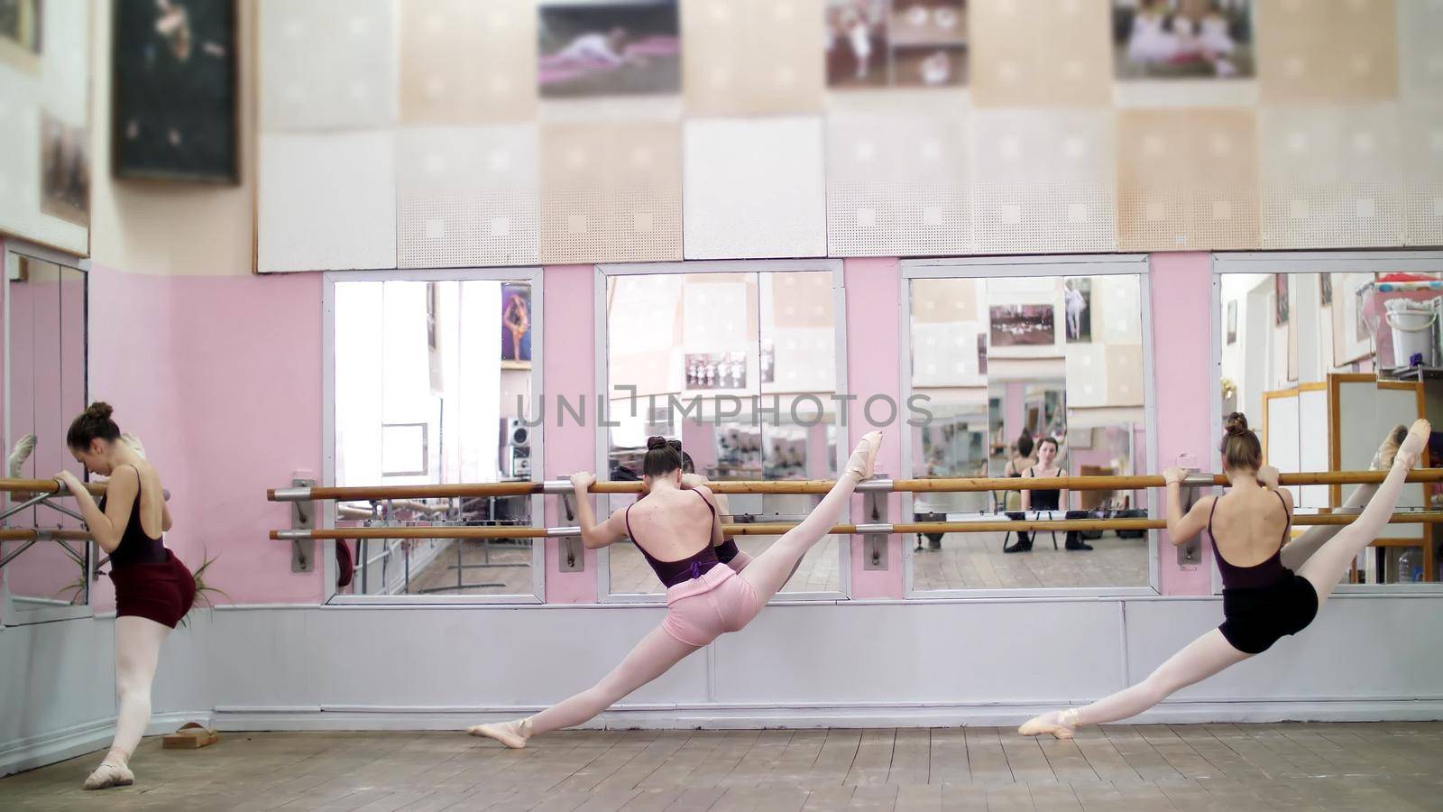 in dancing hall, Young ballerinas in black leotards stretching at barre, on pointe shoes, elegantly, standing near barre at mirror in ballet class. High quality photo