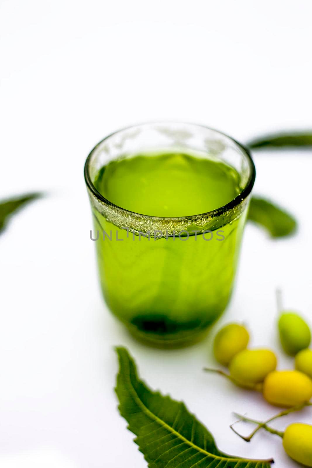 Detox or detoxifying drink of neem fruit in a glass isolated on white along with some neem fruit or nimbodi or nimbudi in a glass bowl.Vertical shot. by mirzamlk