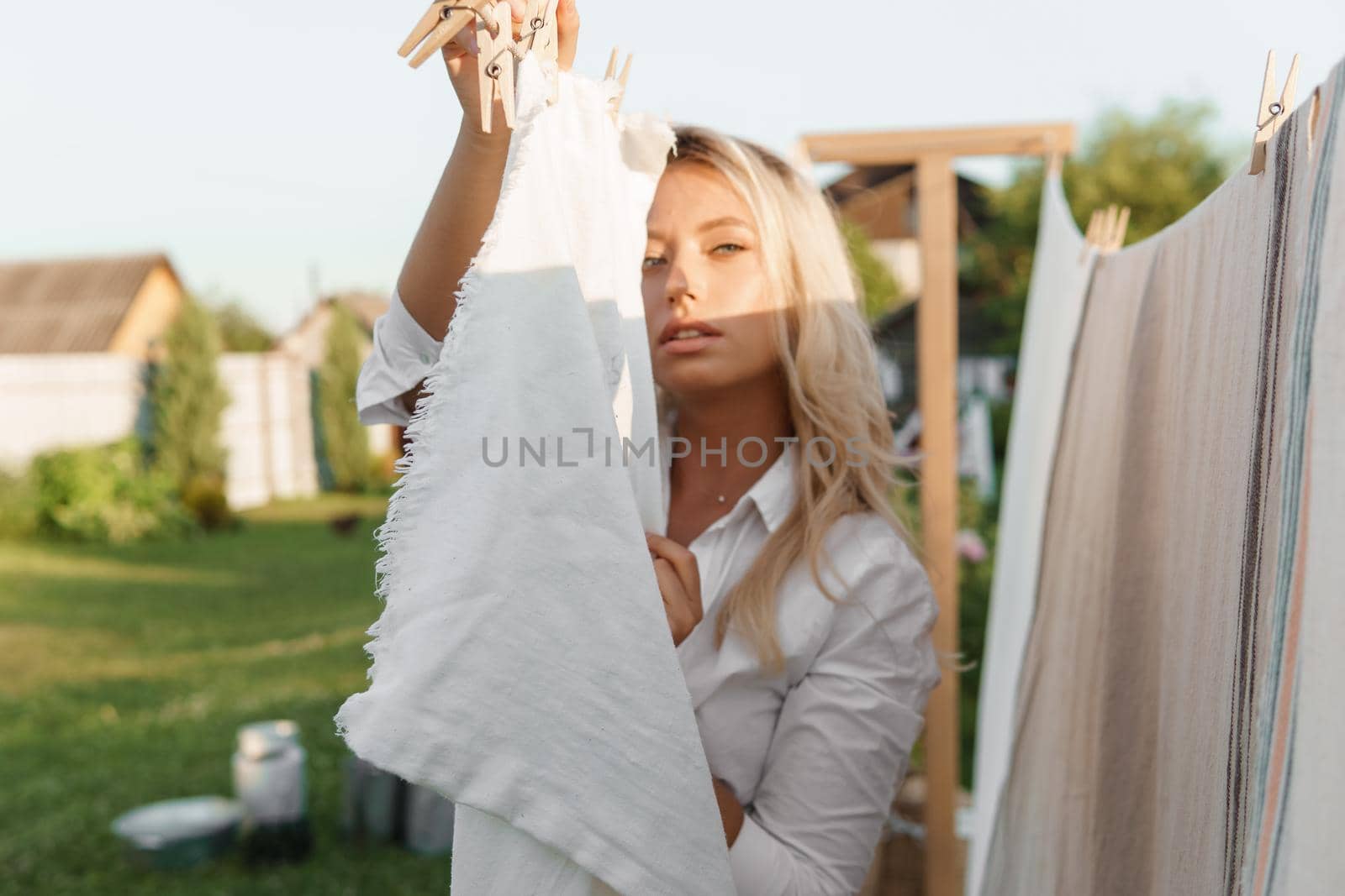 Laundry day. A woman hangs linen and towels on a tree in the courtyard of a village house. Summer cottage concept.