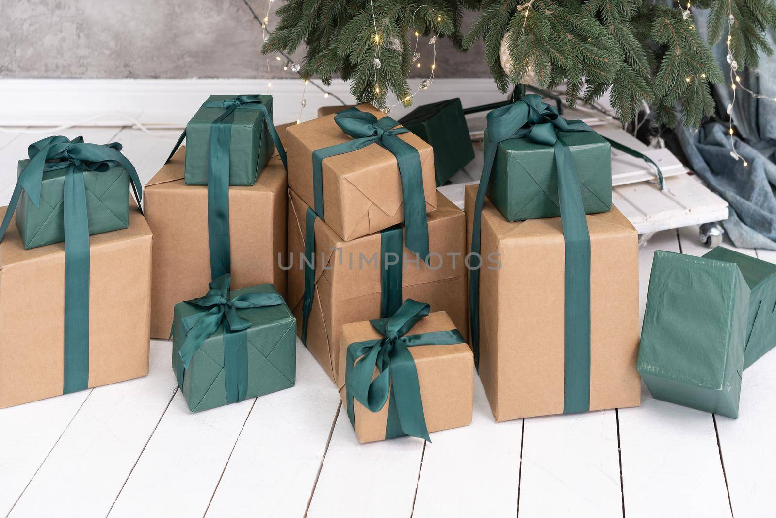 New Year gifts under Christmas tree. Boxes packed in craft and green paper at white floor. Atmosphere of festive surprise by LipikStockMedia