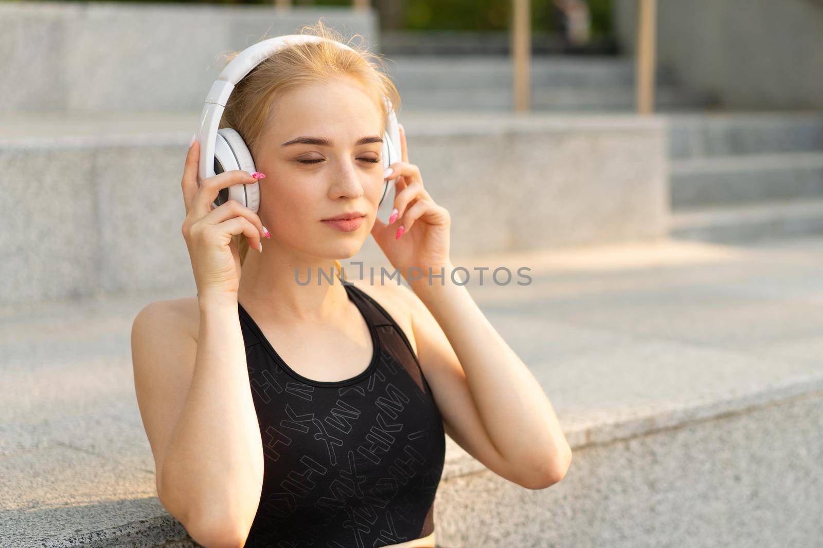 Sport and Fitness Young Adult Caucasian Woman Resting after morning Workout Outdoor Summer Park Athletic Female Take a Break listen Music Headphones