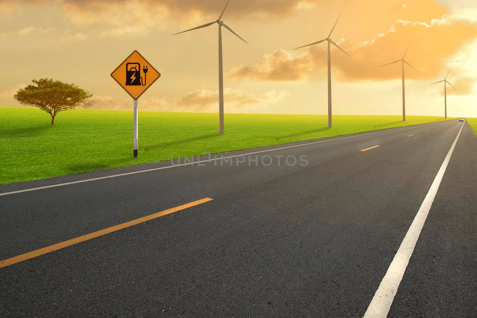 Road in green field and Electric car road sign charging station with wind turbines backgrounds. by thanumporn