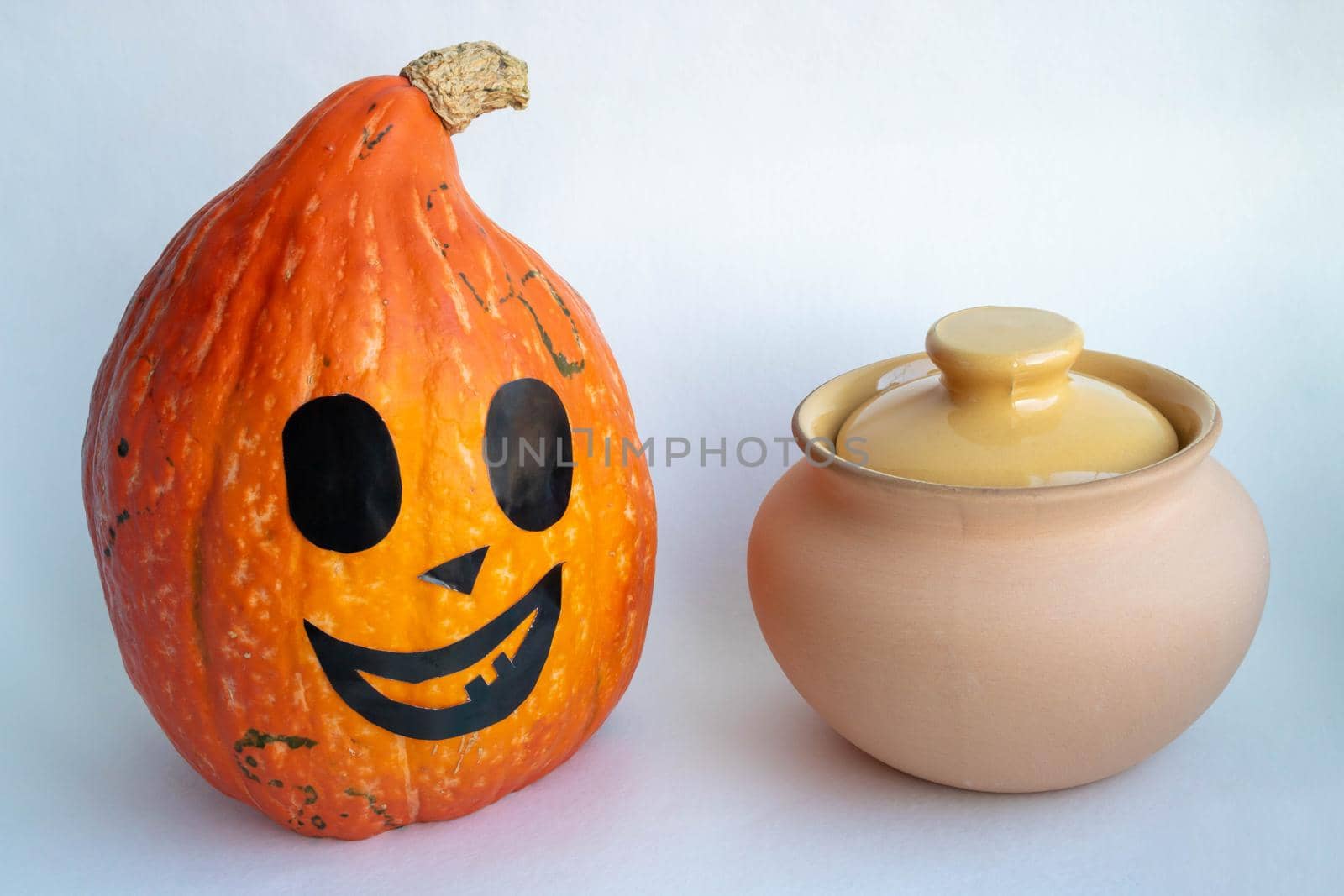 A smiling orange pumpkin next to a clay pot on a white background. Halloween Concept by lapushka62