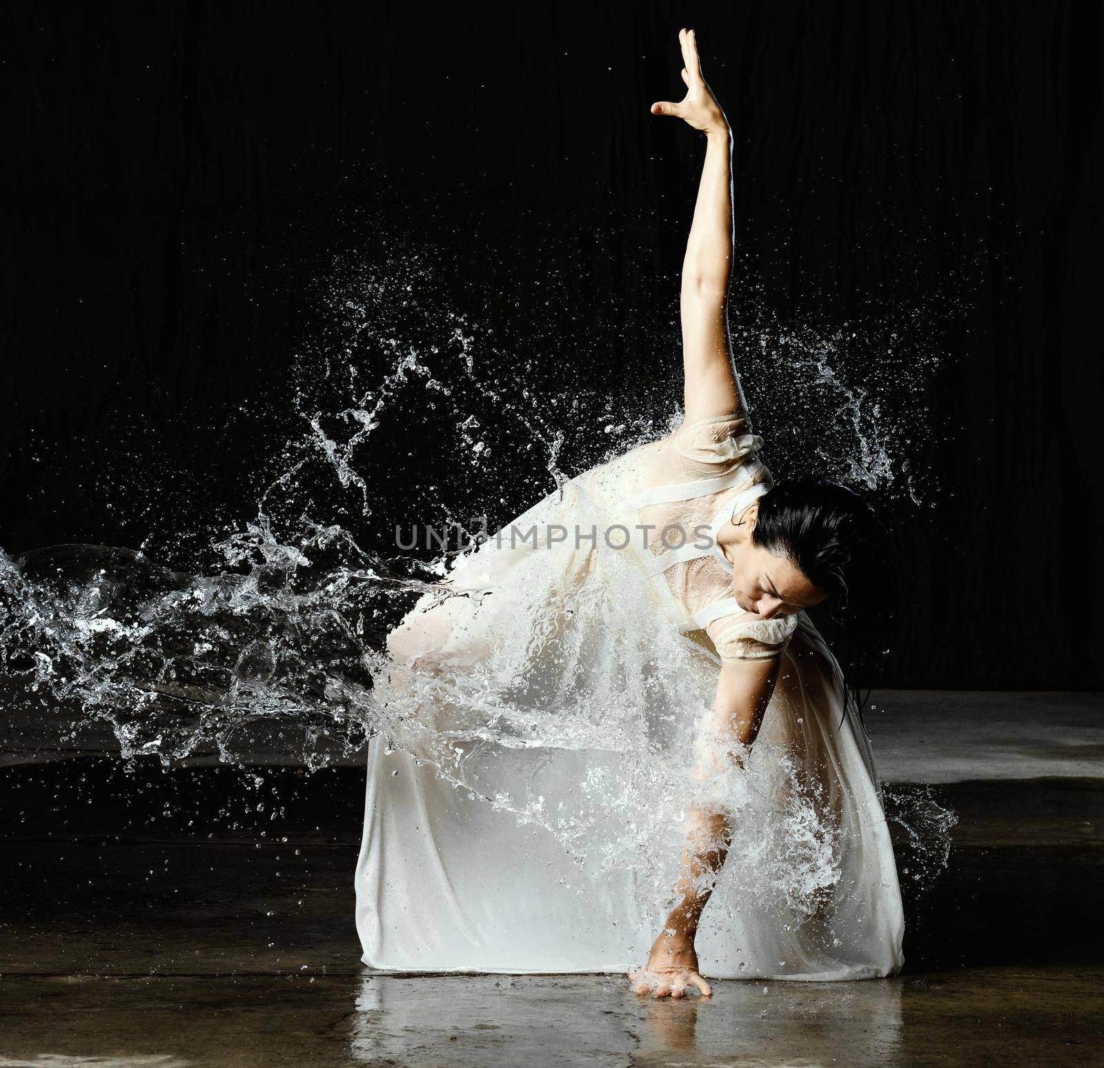 beautiful woman of Caucasian appearance with black hair dances in drops of water on a black background. The woman is wearing a white chiffon dress by ndanko