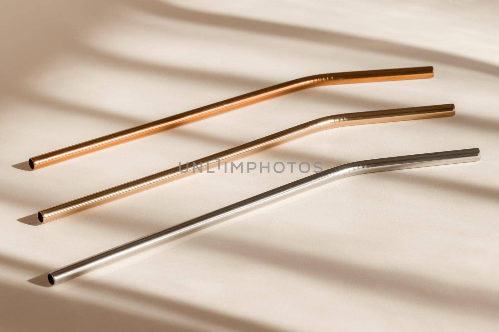Sustainability concept. Eco friendly drinking straws from aluminium or stainless steel, reusable zero waste metal straw on neutral beige background with shadow from room windows by photolime