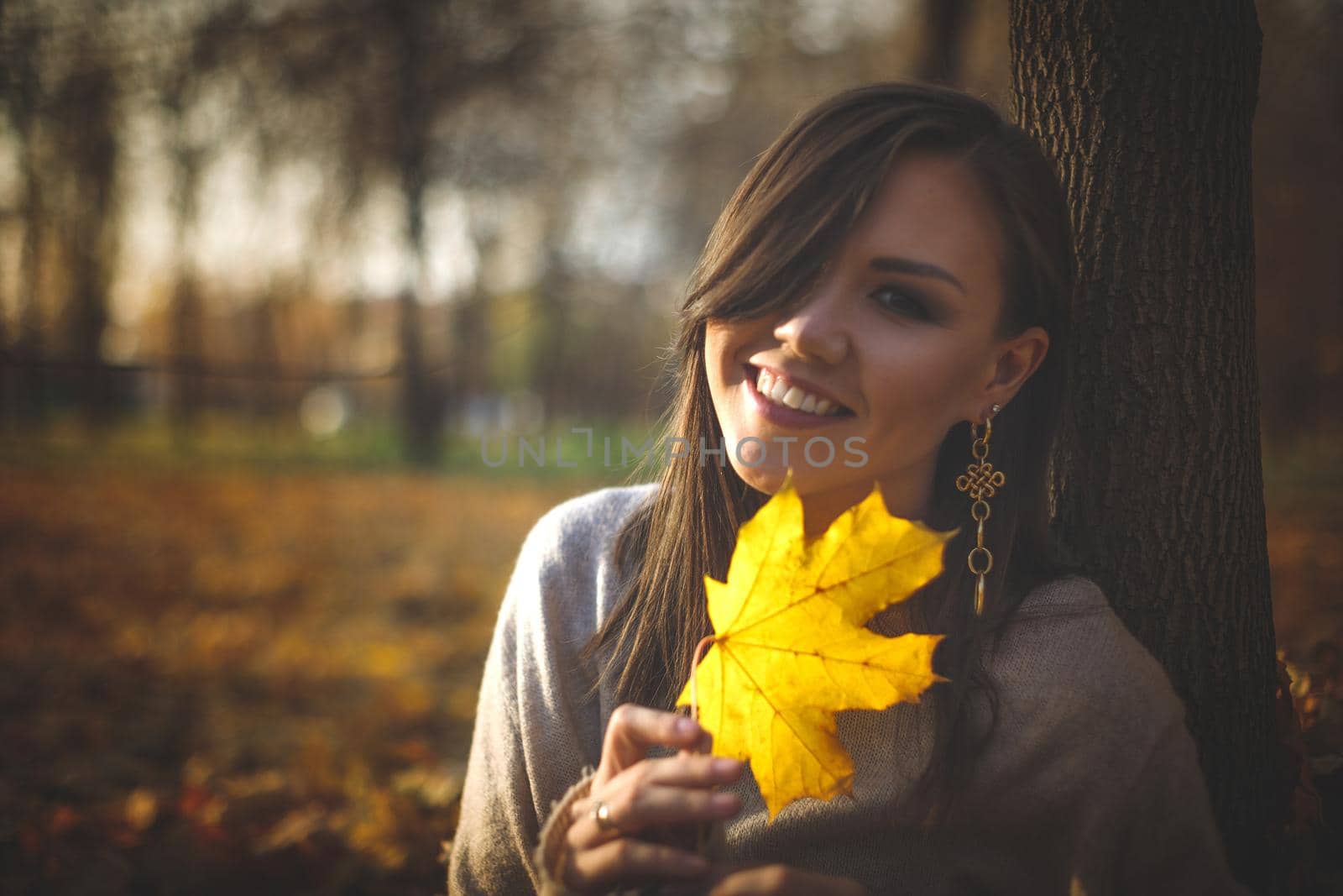 Portrait of a young Central Asian woman with a yellow maple leaf in her hands in the evening autumn park.