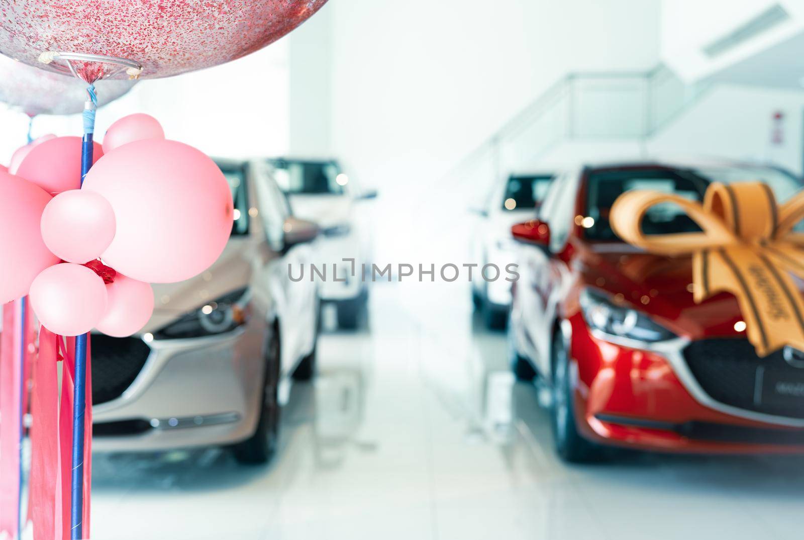 Pink balloons on blur car parked in luxury showroom. New car parked in modern showroom. Car dealership office. Automobile leasing and insurance concept. Auto leasing business. Electric vehicle dealer. by Fahroni