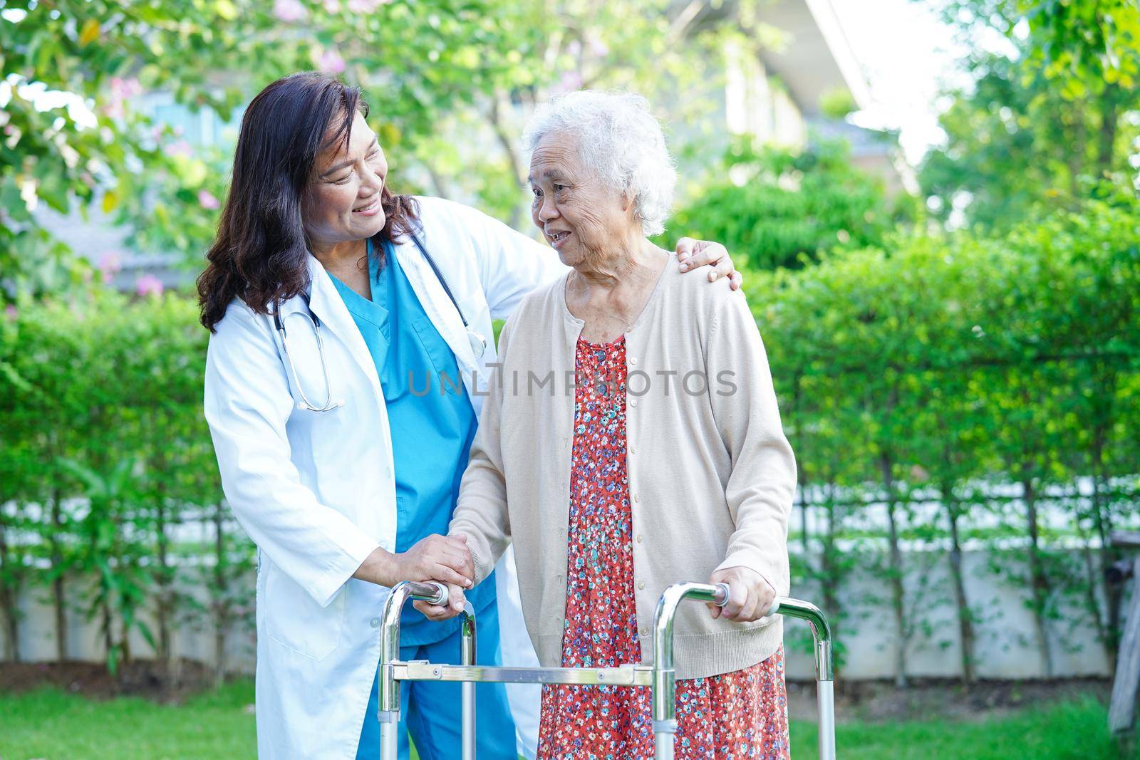 Doctor help Asian elderly woman disability patient walk with walker in park, medical concept.