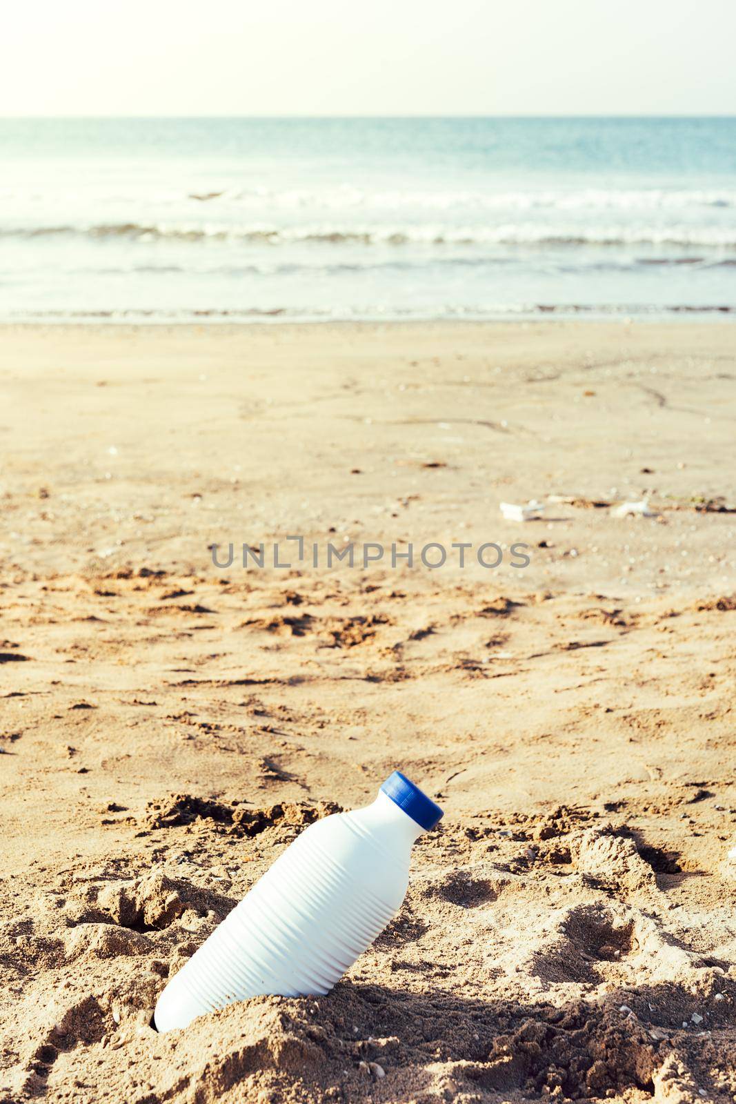vertical photo of a white plastic bottle lying on the sand of the beach and pollutes the sea and the marine life, concept of pollution control of the oceans by plastic