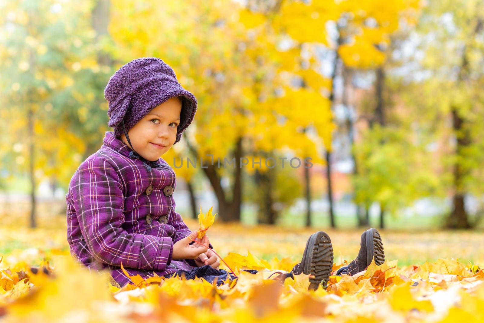 Caucasian little girl of five years old sitting on ground with yellow leaves in autumn park