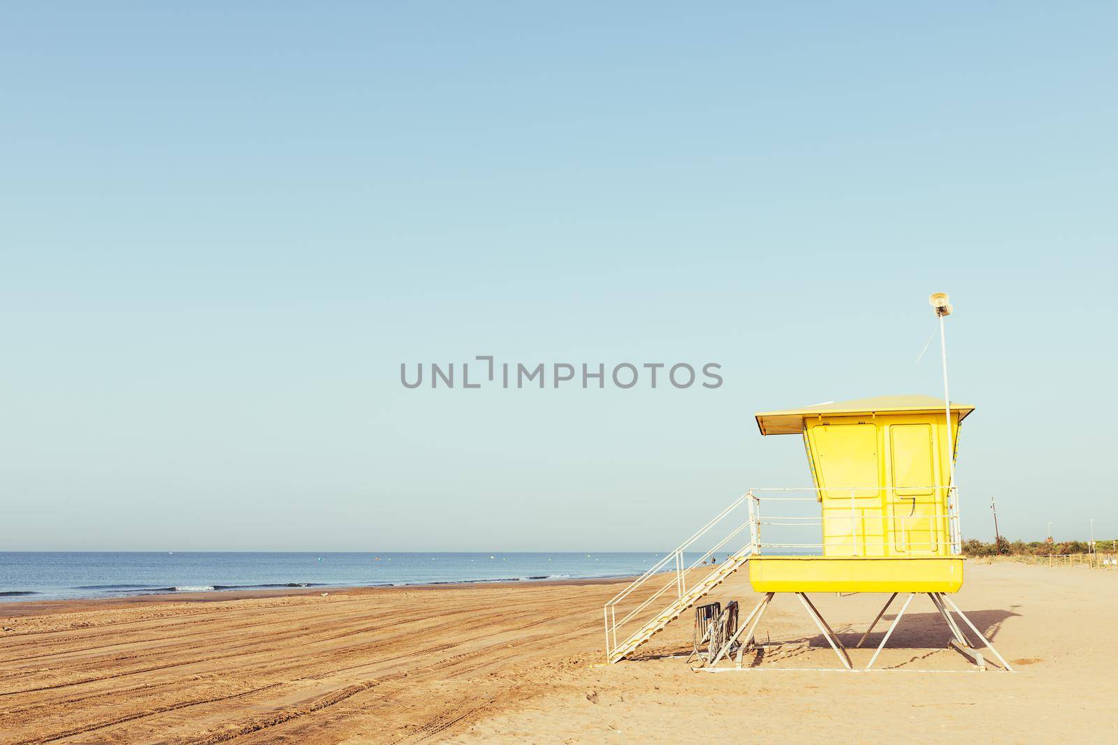 summer scene with a colorful yellow lifeguard tower on the beach, at sunset with clean sky in the background, copy space for text