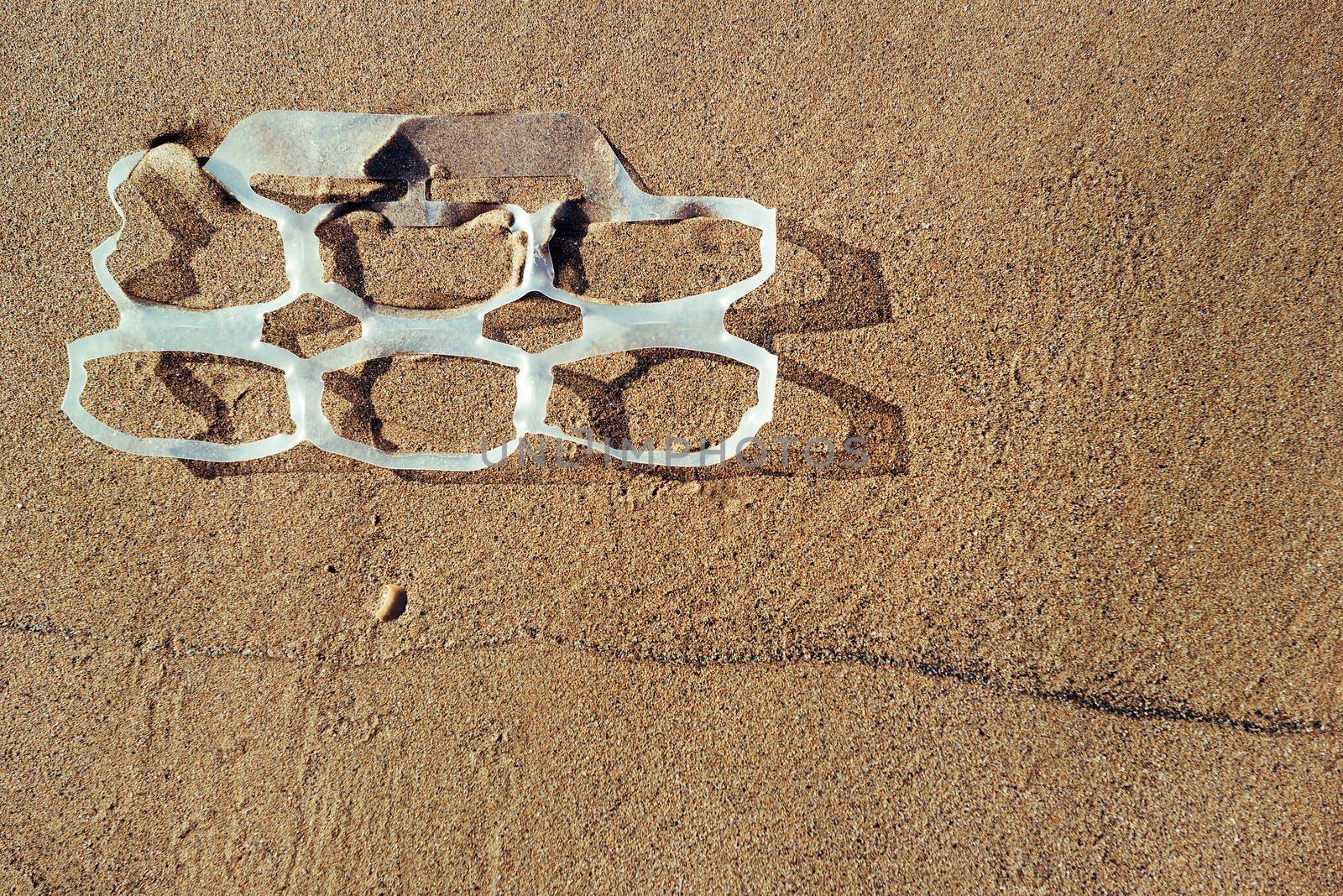 background of a plastic rings lies on the sand of the beach and pollutes the sea and the marine life, concept of pollution control of the oceans by plastic, copy space for text