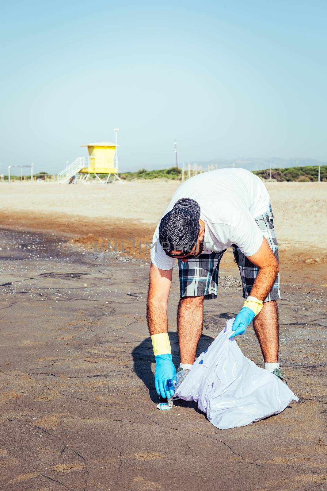 man collecting waste that pollute the ocean in plastic bag, people helping to keep nature clean and picking up the plastics from beach, volunteer campaign to cleaning on the beach, vertical photo