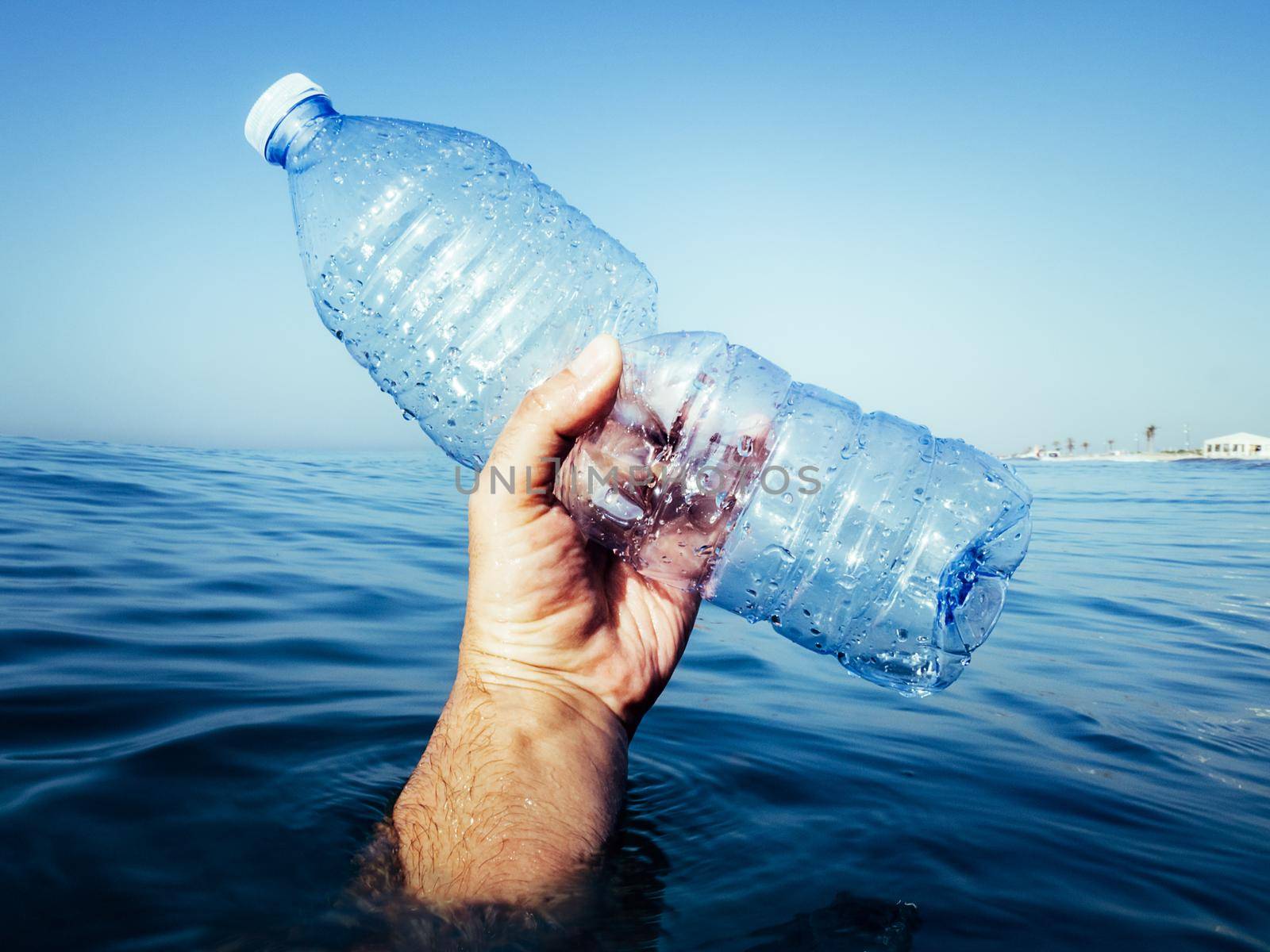 plastic waste at the ocean, hand coming out of the water holding a plastic bottle in the Mediterranean sea, environmental problem with plastics pollution, copy space for text