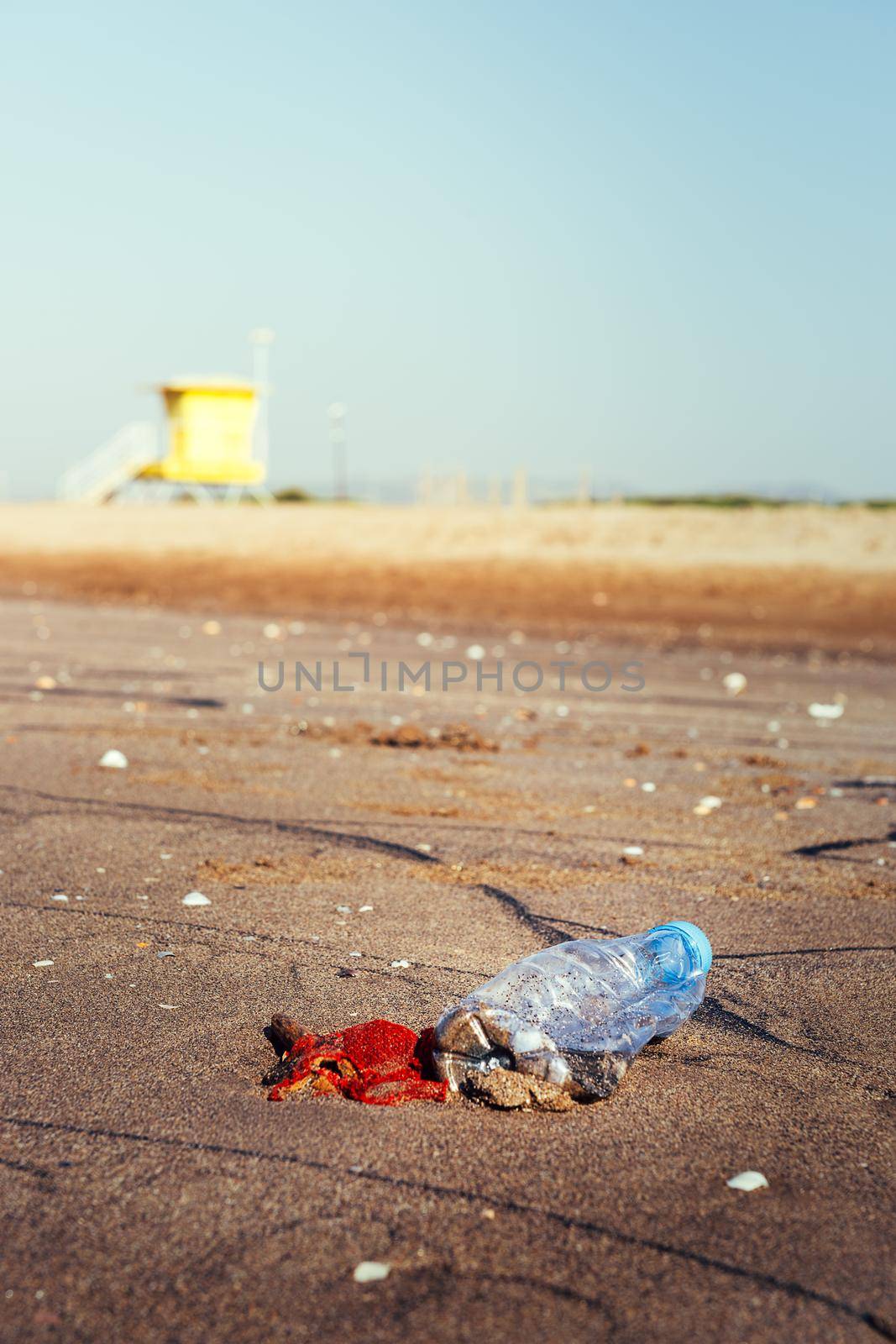 vertical photo of a plastic bottle and garbage lies on the sand of the beach polluting the sea and the marine life, concept of pollution control of the oceans by plastic