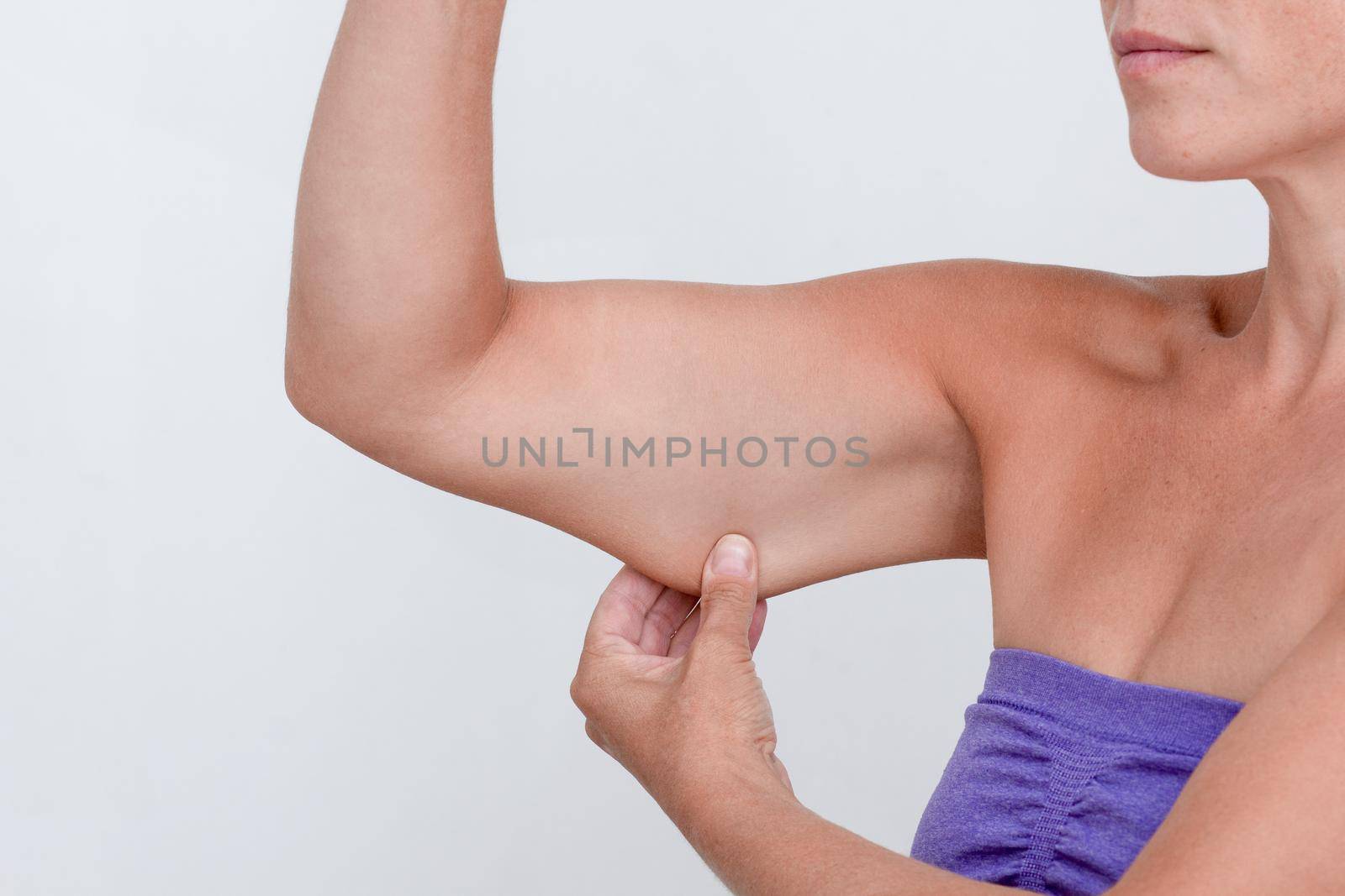 Cropped woman body showing arm with sagging skin on grey background