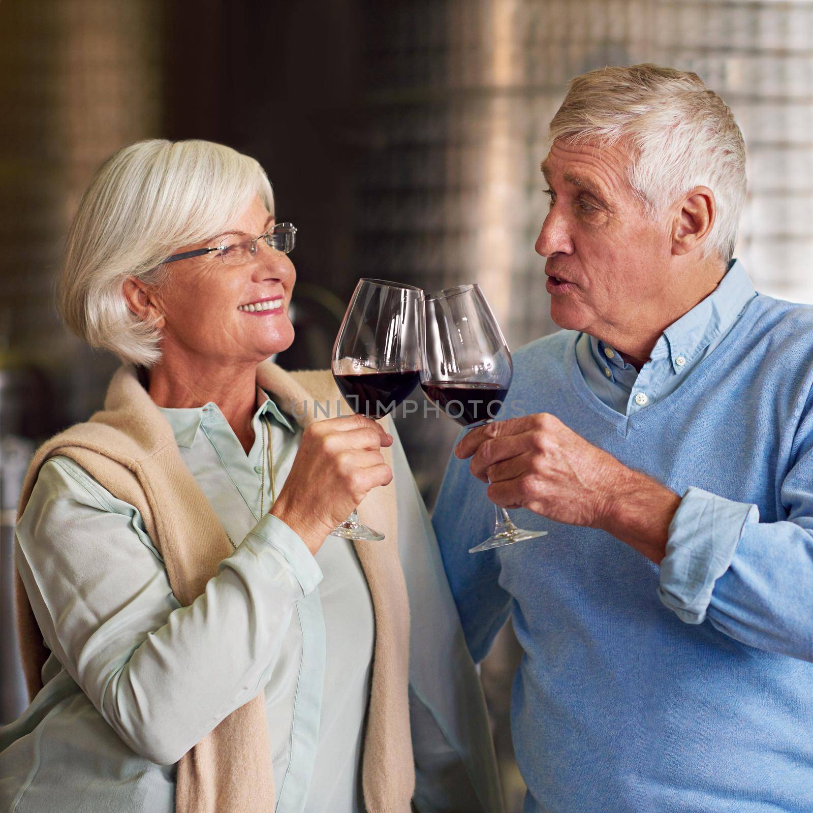 Cheers. an affectionate senior couple wine tasting in a cellar. by YuriArcurs