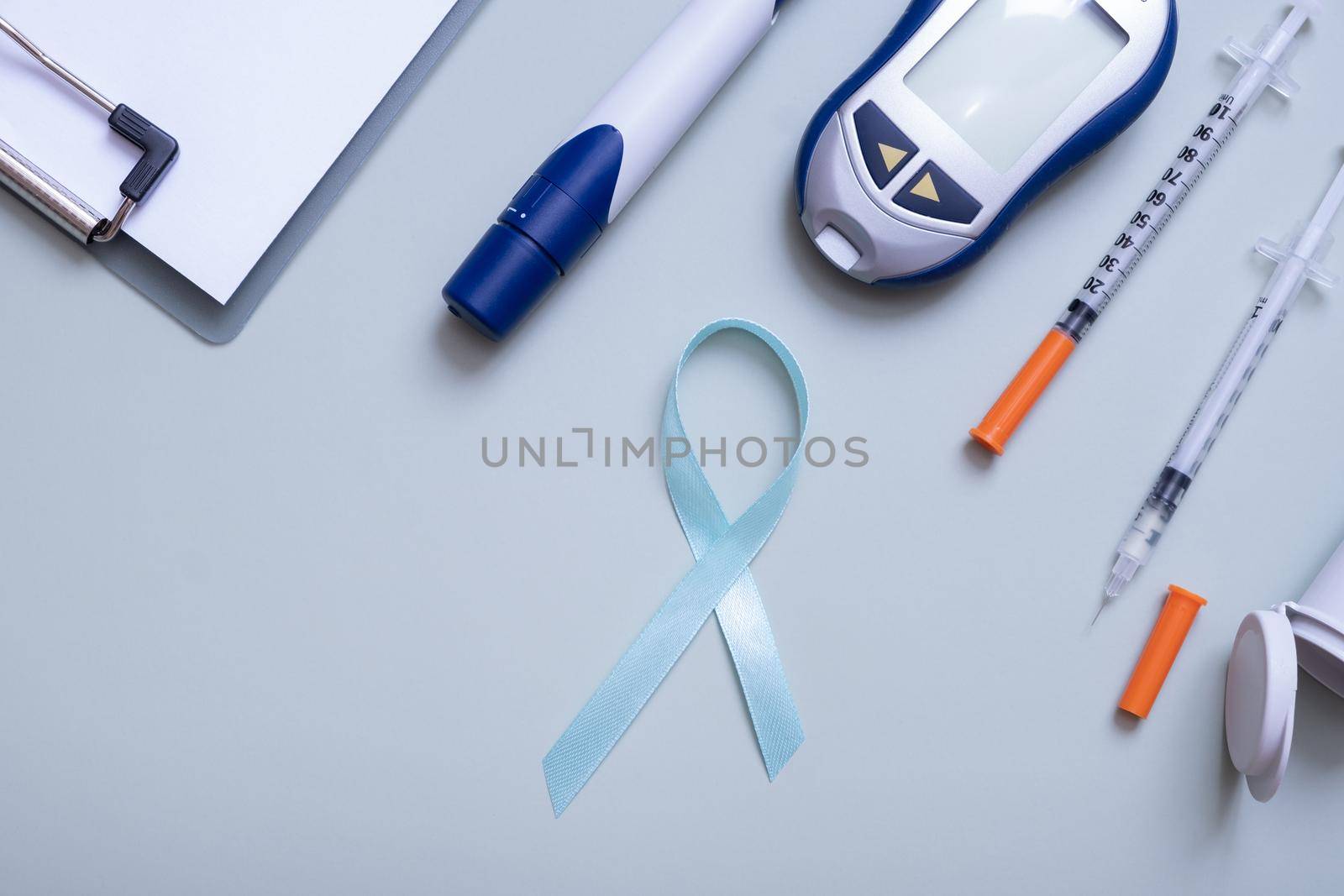Blue ribbon and glucometer, medical supplies on color background top view with copy space. World diabetes day concept.