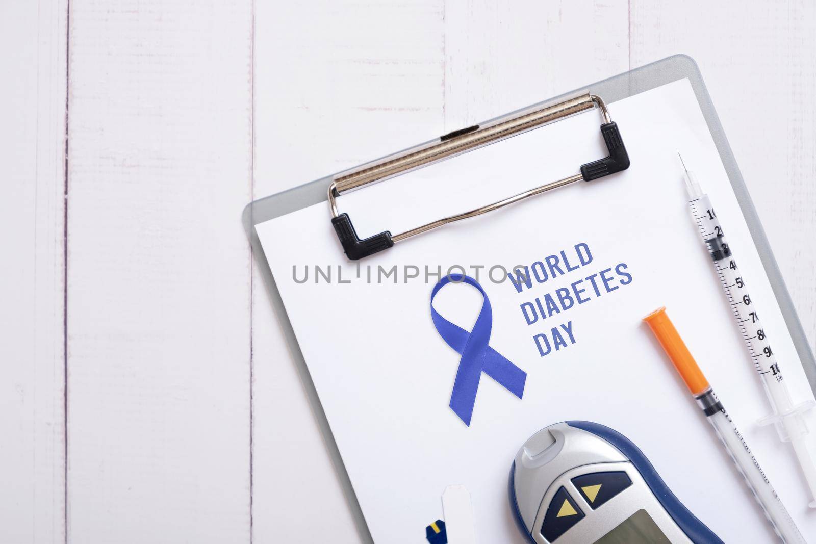 Text World Diabetes Day and blue ribbon on tablet with glucometer and syringes on a wooden background, top view by ssvimaliss