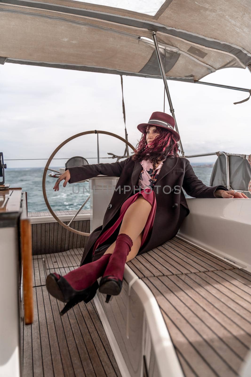 Attractive middle-aged woman at the helm of a yacht on a summer day. Luxury summer adventure, outdoor activities. by Matiunina