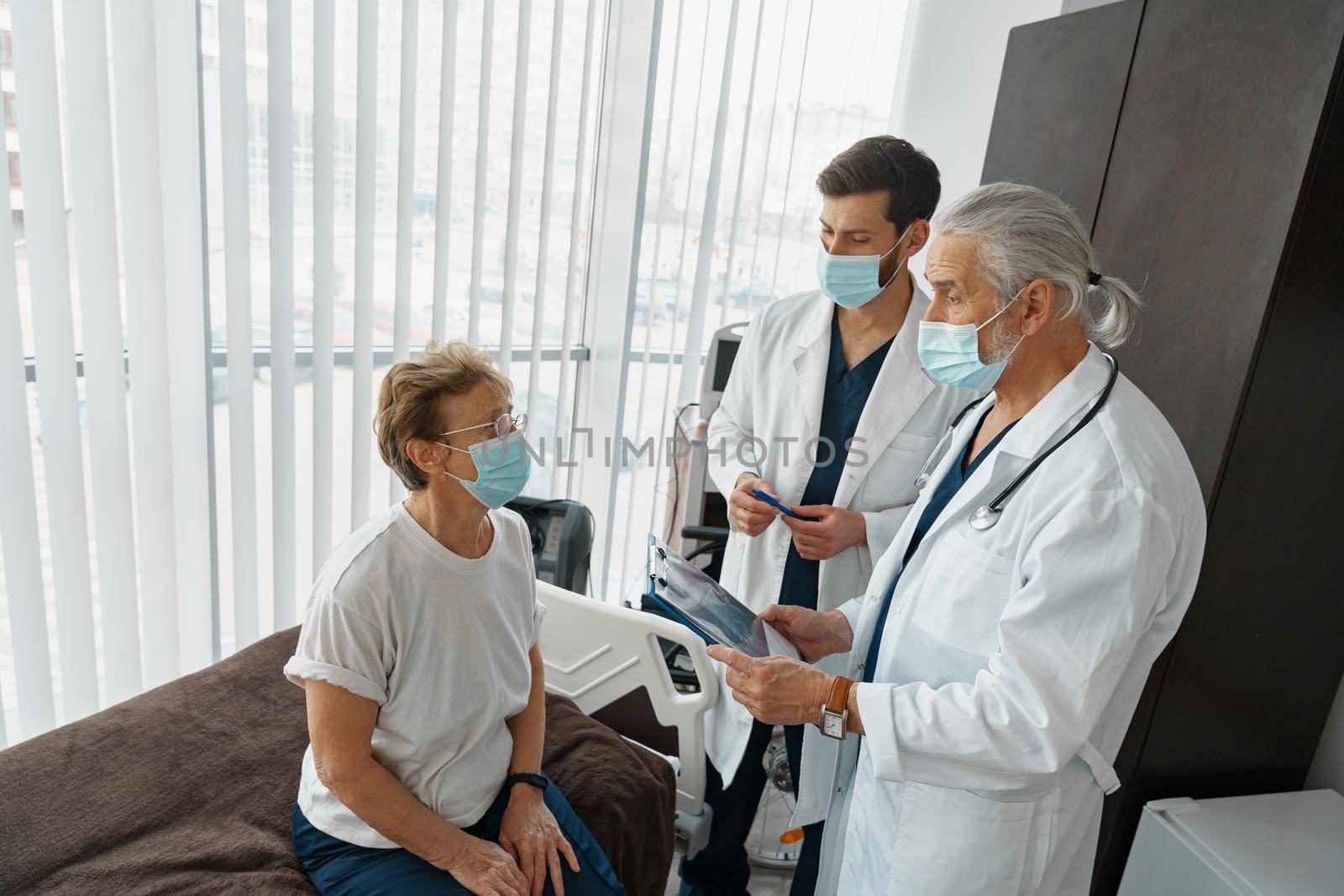 Doctors in masks explain to a sick patient in a wheelchair her diagnosis . High quality photo