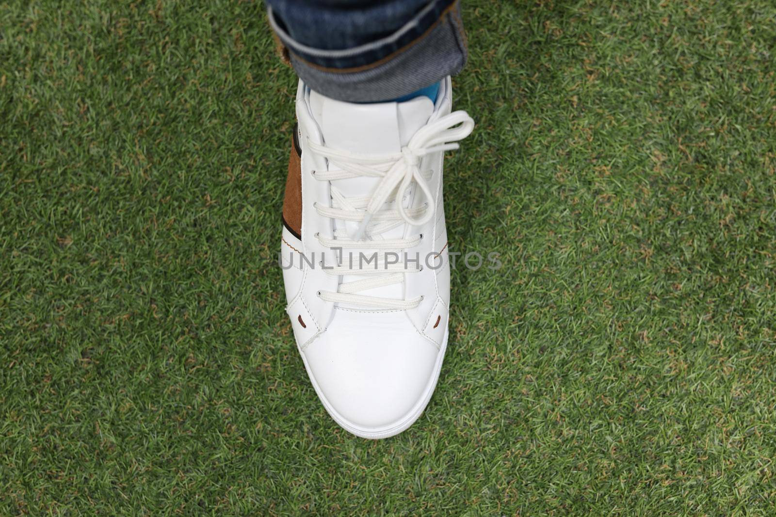 Man is wearing white sneakers on green lawn grass by kuprevich