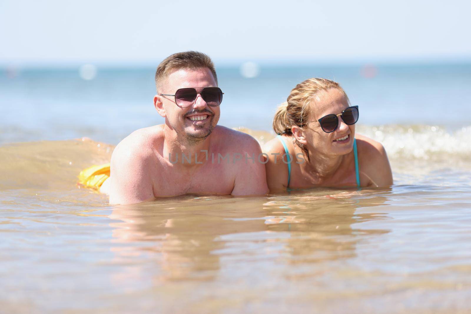 Happy couple in sunglasses lies on beach in sea. Sea summer vacation emotions and romantic trips