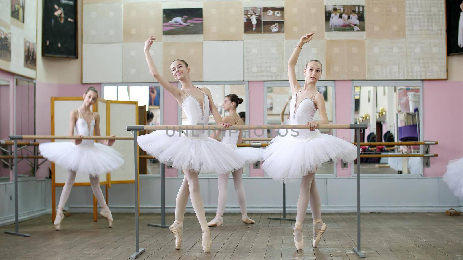 in the ballet hall, girls in white ballet tutus, packs are engaged at ballet, rehearse croise forward, Young ballerinas standing on toes in pointe shoes at railing in ballet hall. by djtreneryay