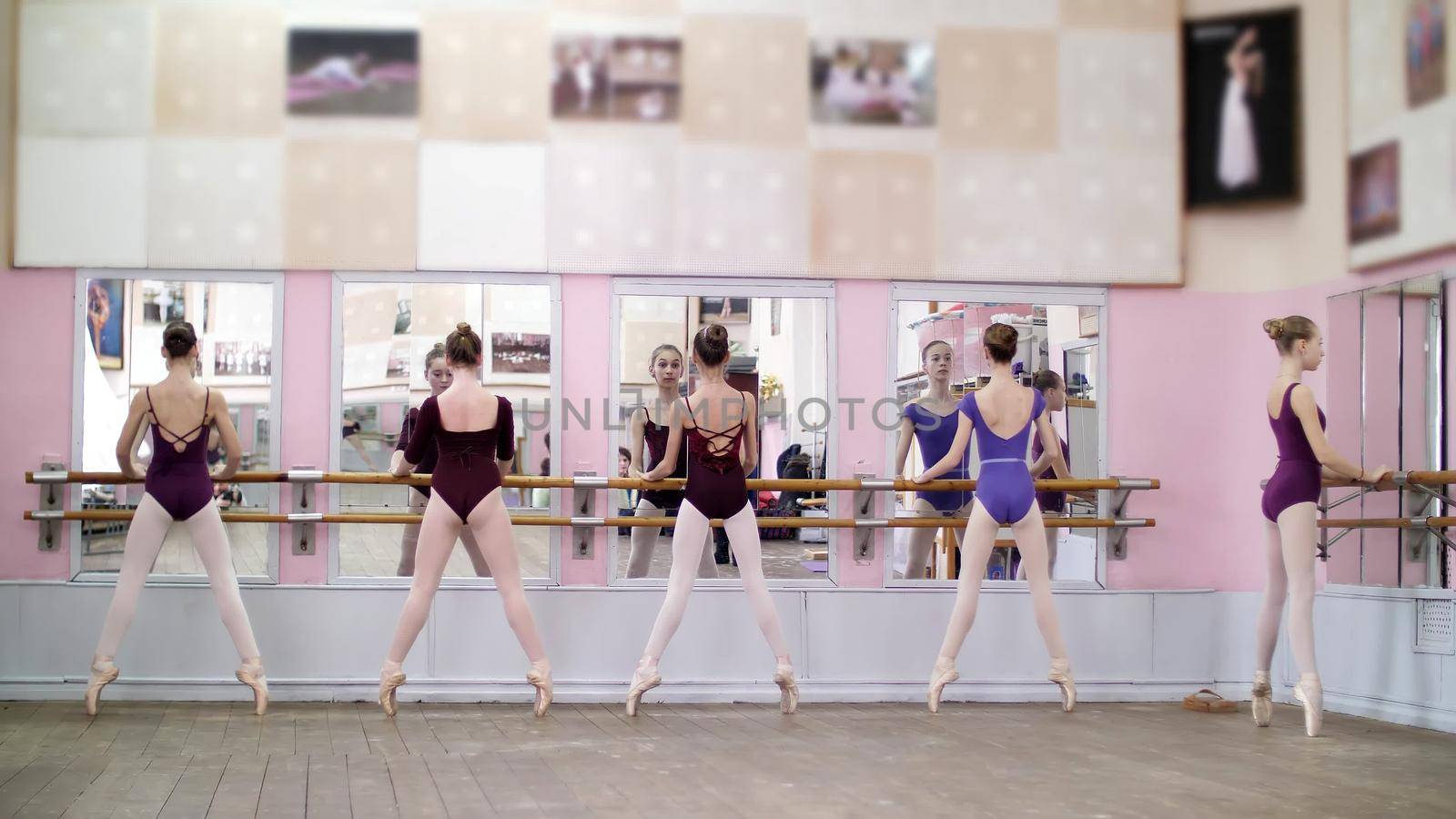in ballet hall, Young ballerinas in purple leotards perform pas eshappe, going up, standing on toes in pointe shoes at railing in ballet hall. High quality photo