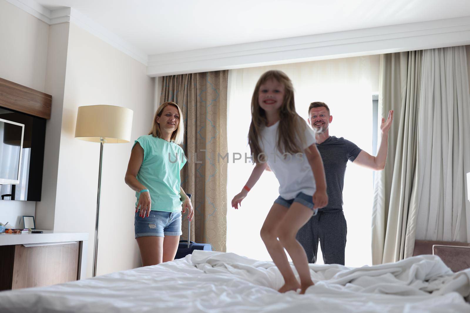 Happy family mother father and child laughing play and jump in bed in bedroom at home or hotel. Family emotions love and joy