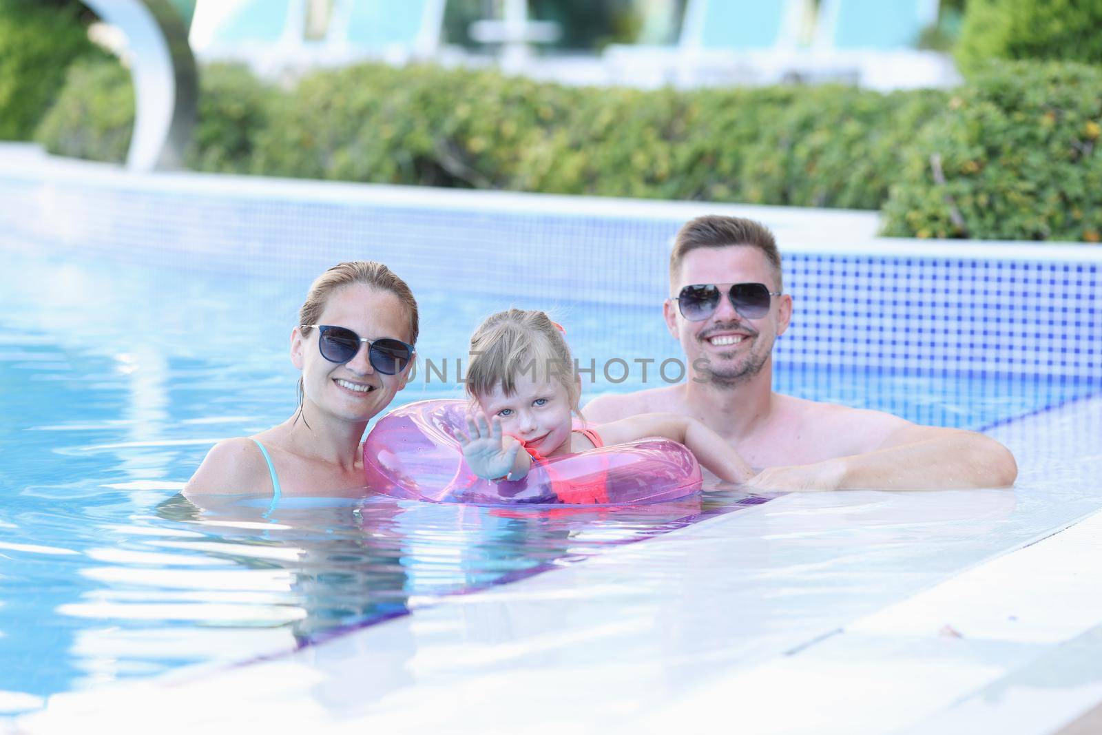 Portrait of young family with smiling child in pool. Happy joyful family together in pool