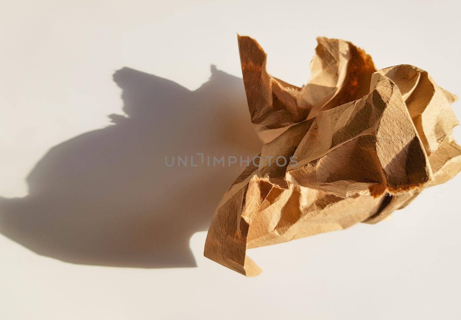 A crumpled paper ball made of brown kraft paper and its shadow on a light background, top view.