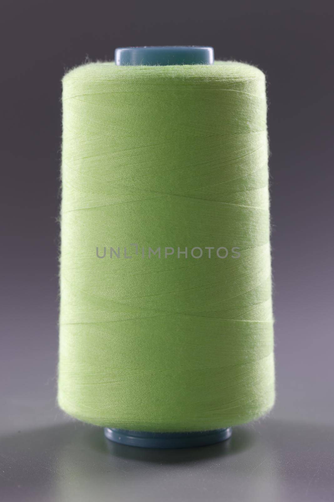 Light green spool of thread on gray background. Sewing machine materials and high-quality durable threads