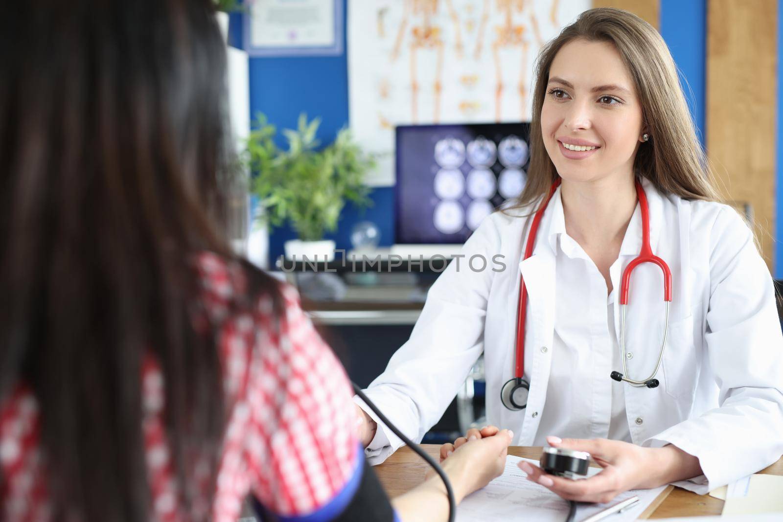 Beautiful female doctor working with patient measures blood pressure. Doctor uses tonometer to measure blood pressure of young woman and takes notes